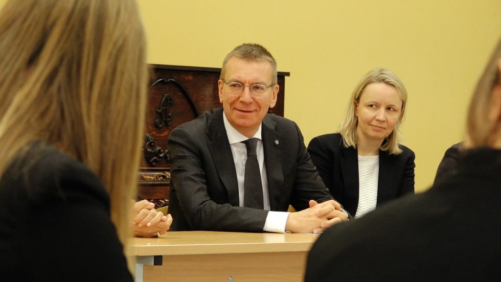 Valsts prezidents Edgars Rinkēvičs smaidot sēž pie galda un sarunājas ar jauniešiem un darbiniekiem telpā ar dzeltenām sienām.