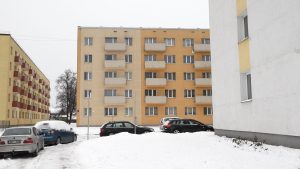 Daudzdzīvokļu dzīvojamās mājas ziemā ar sniegu klātu pagalmu un stāvvietu