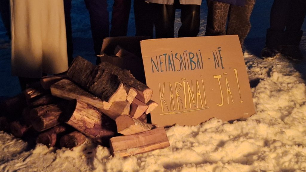 Uz sniega blakus malkas grēdai novietots kartona plakāts ar uzrakstu "NETAISNĪBAI - NĒ, KARĪNAI - JĀ!".
