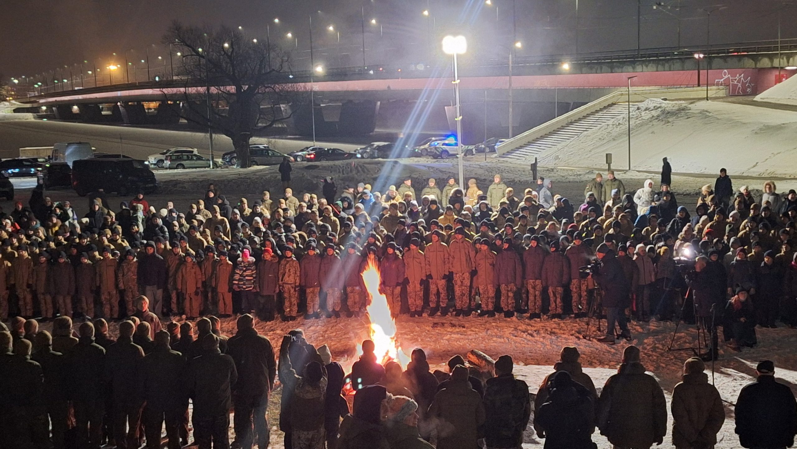 Skats no augšas uz simtiem jaunsargu un iedzīvotāju, kas tumsā aplī ielenkuši piemiņas ugunskuru pie televīzijas torņa Zaķusalā.