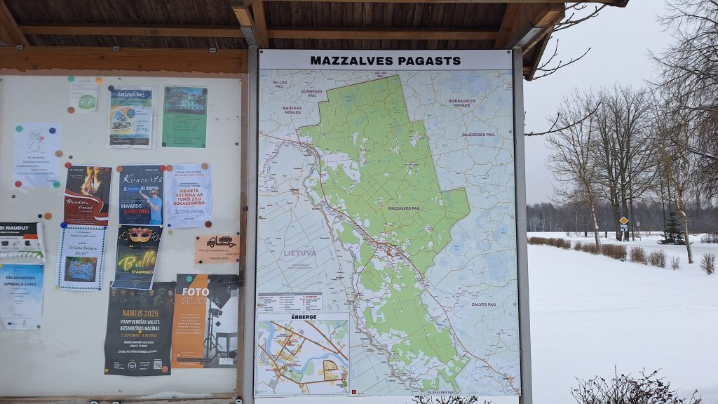 Informācijas stends ārā ar Mazzalves pagasta karti un dažādiem paziņojumiem un afišām.
