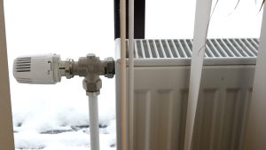 Apkures radiators ar termoregulatoru pie loga ziemas laikā