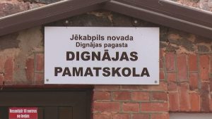 Zīme ar uzrakstu “Jēkabpils novada Dignājas pagasta Dignājas pamatskola” pie skolas ēkas ieejas