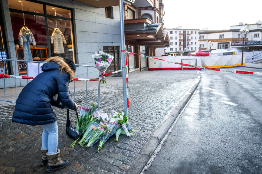 Cilvēki noliek ziedus pie norobežotas ugunsgrēka vietas Šveices kūrortā Kranmontanā