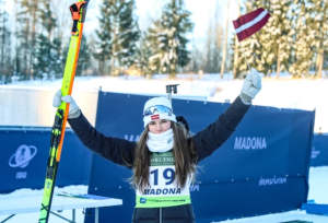 Latvijas biatloniste Estere Volfa finišā Madonā paceļ slēpes un tur Latvijas karodziņu, svinot uzvaru IBU junioru kausa posmā.