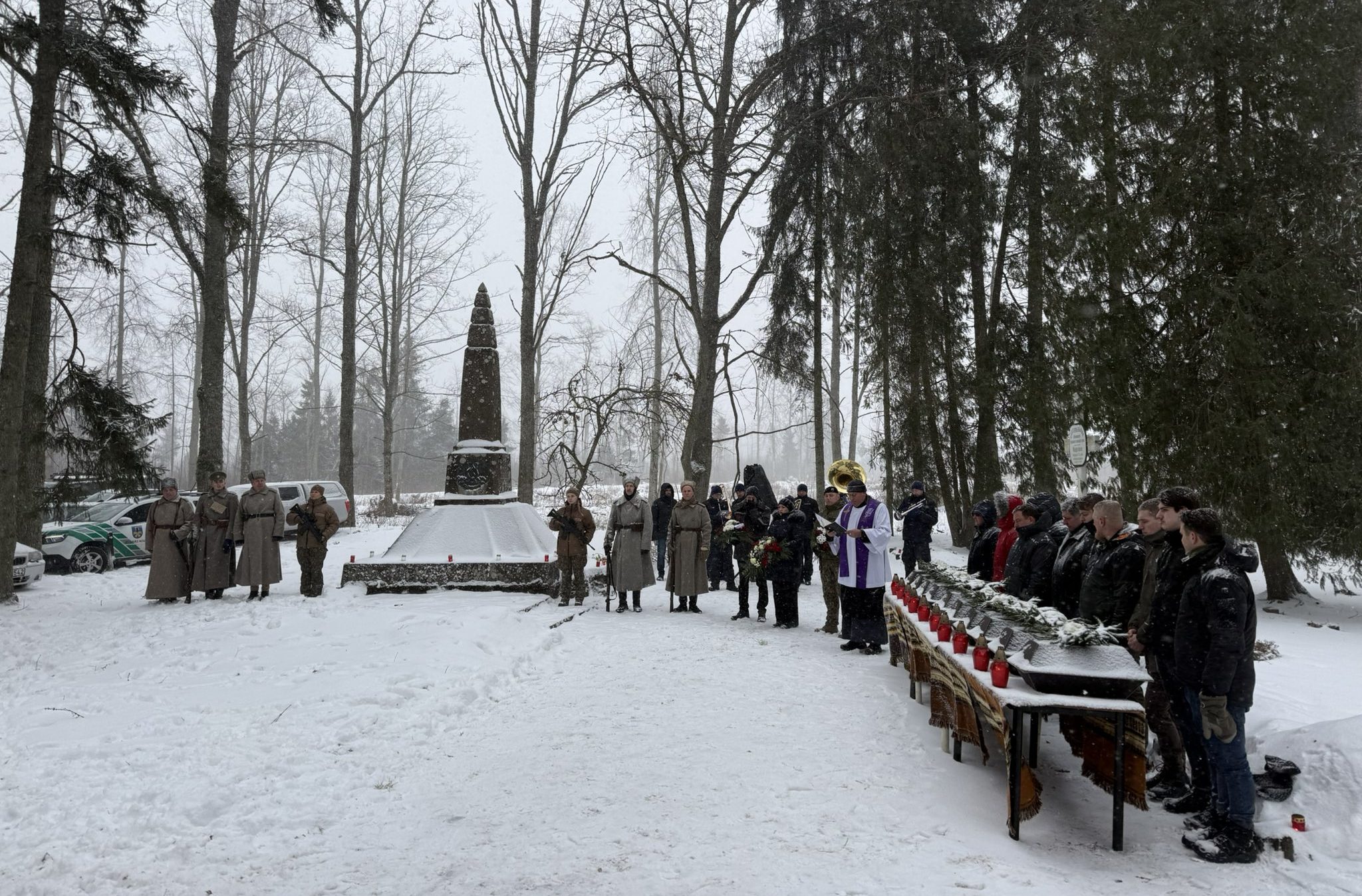 Piemiņas pasākums sniegotā mežā pie pieminekļa ar karavīriem vēsturiskos tērpos un mācītāju.
