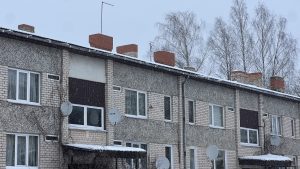 Daudzdzīvokļu dzīvojamā māja ziemā ar sniegu uz jumta un satelītantennām pie logiem