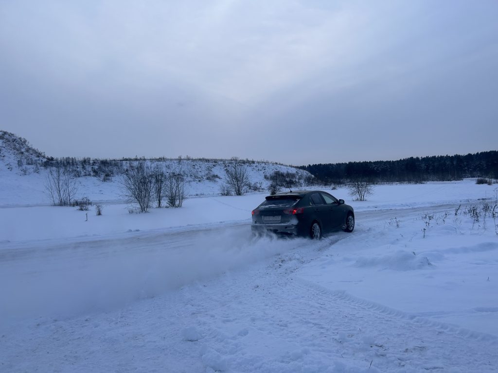 Tumši zaļa automašīna veic sānslīdi pa apsnigušu un aplejojošu trasi Jēkabpilī, aiz sevis paceļot sniega mākoni.