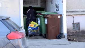 Cilvēks pie atkritumu konteineriem daudzdzīvokļu mājas pagalmā