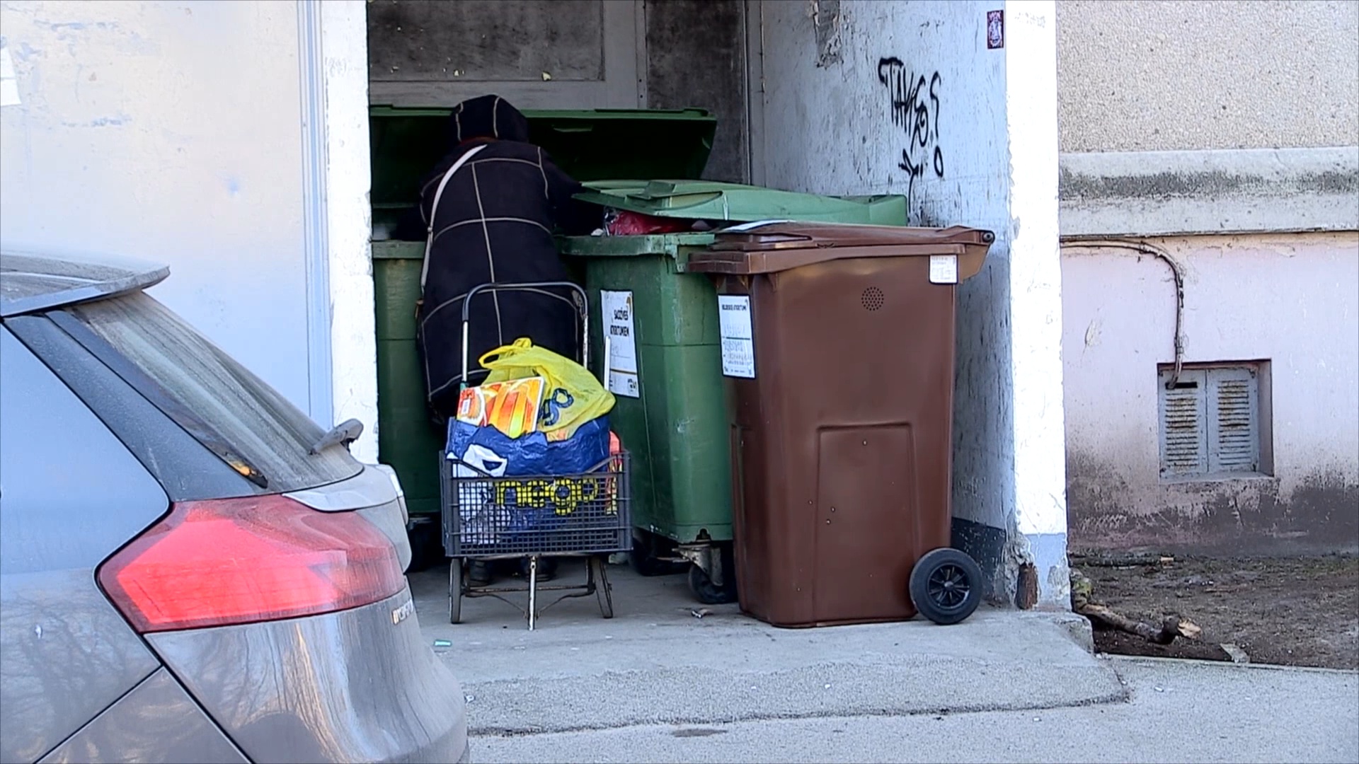 Cilvēks pie atkritumu konteineriem daudzdzīvokļu mājas pagalmā