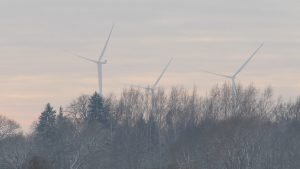 Vēja elektrostacijas virs koku galotnēm ziemas ainavā