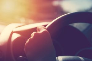 Autovadītāja roka uz stūres saulainā laikā, simbolizējot drošu braukšanu un KASKO apdrošināšanu