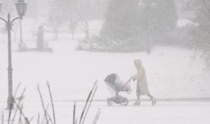 Cilvēks sniegputenī stumj bērnu ratiņus parkā
