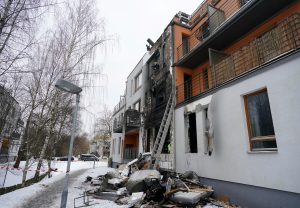 Daudzdzīvokļu mājas fasāde ar melnām deguma pēdām, izsistiem logiem un gruvešu kaudzi pie ēkas sienas ziemā.