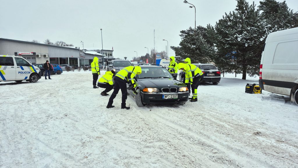 Valsts policijas inspektors un CSDD darbinieks Jēkabpilī veic apturētas automašīnas tehnisko pārbaudi ceļa malā.