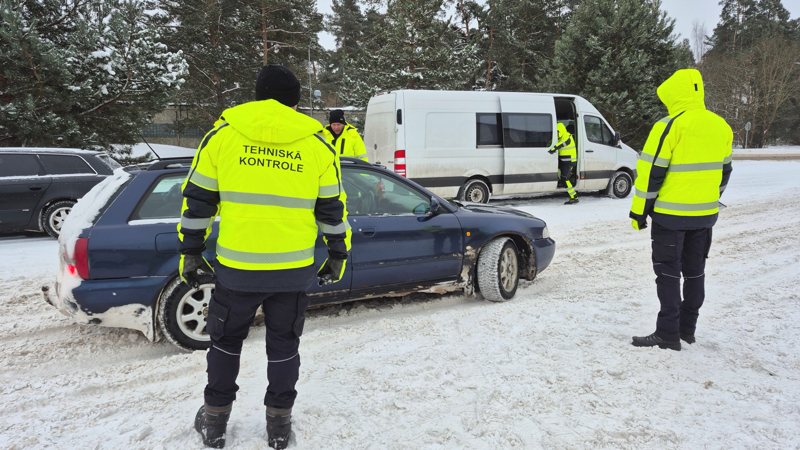 Valsts policijas inspektors un CSDD darbinieks Jēkabpilī veic apturētas automašīnas tehnisko pārbaudi ceļa malā.