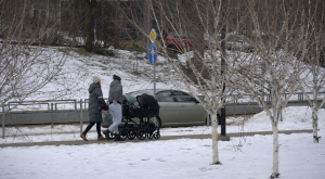 Jauna ģimene ar bērnu ratiņiem ziemā dodas pastaigā pilsētvidē.