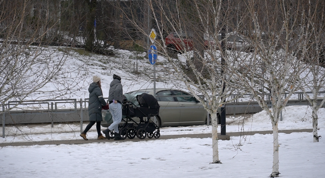 Jauna ģimene ar bērnu ratiņiem ziemā dodas pastaigā pilsētvidē.