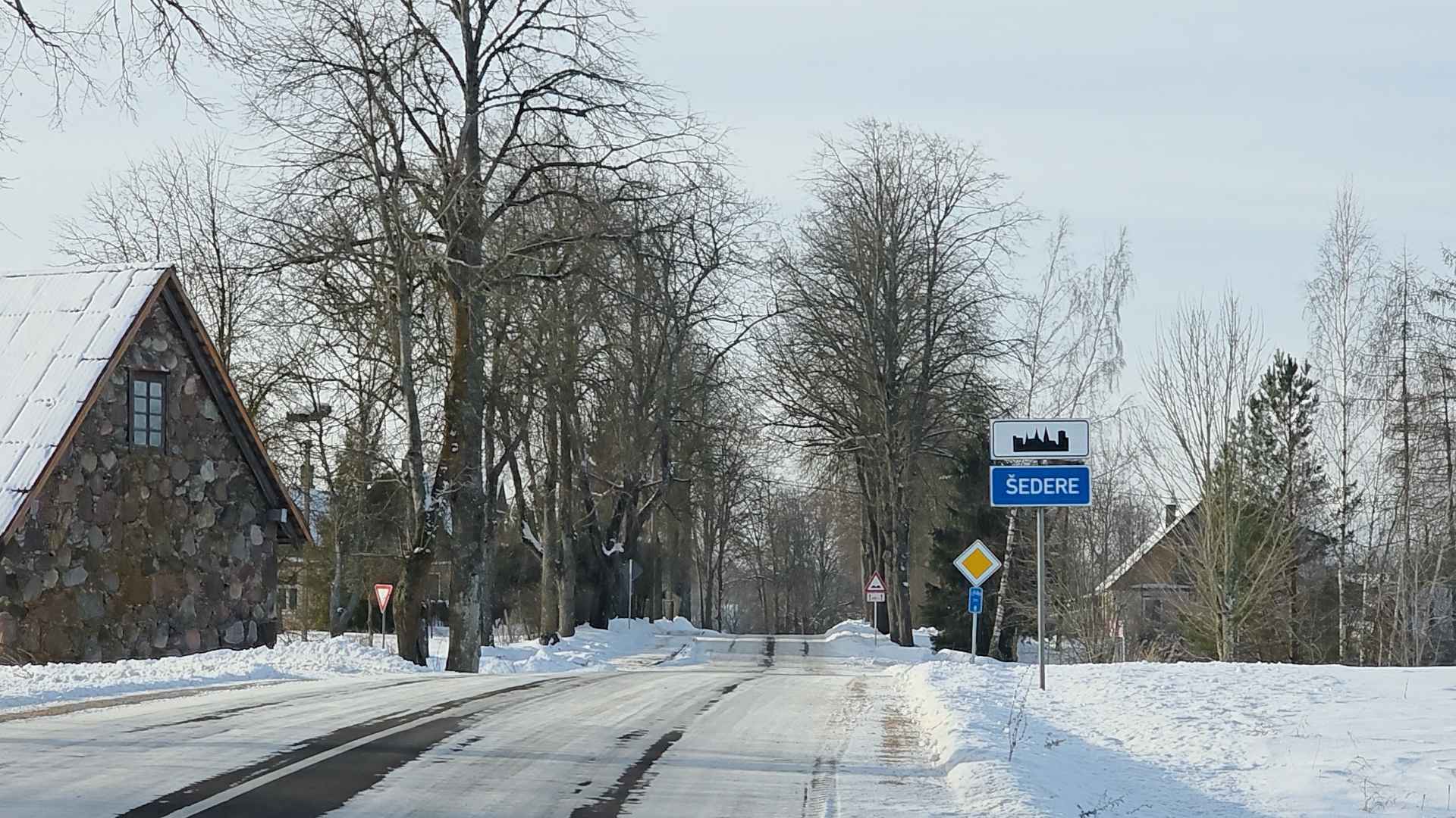 Ceļazīme ar uzrakstu “Sēdere” pie apdzīvotas vietas ziemas apstākļos