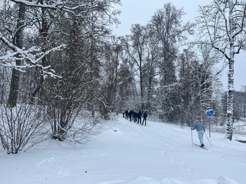 Skats no aizmugures uz slēpotāju rindu, kas dodas pa meža ieloku Dagdas slēpošanas trasē.