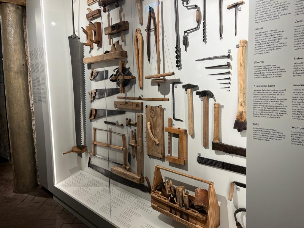 Liela stikla vitrīna ar desmitiem senatnīgu galdniecības un namdara instrumentu.