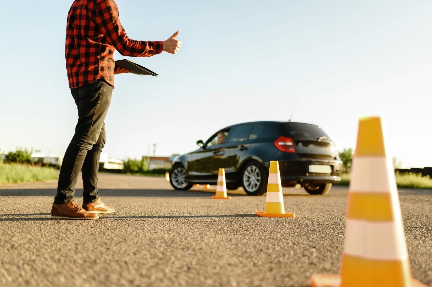 Braukšanas eksāmens autoskolā – instruktors vērtē vadītāja prasmes uz ceļa ar konusiem norobežotā laukumā.