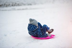Mazs bērns ziemā vizinās ar ragaviņām sniegā