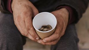 Cilvēks tur krūzīti ar sīknaudu – nabadzības un sociālās atstumtības simbols