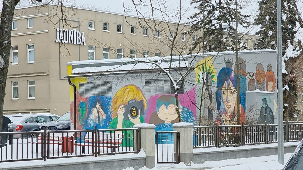 Apgleznots tehnisks objekts pilsētā ar košiem zīmējumiem; fonā redzama ēka ar uzrakstu "JAUNĪBA".