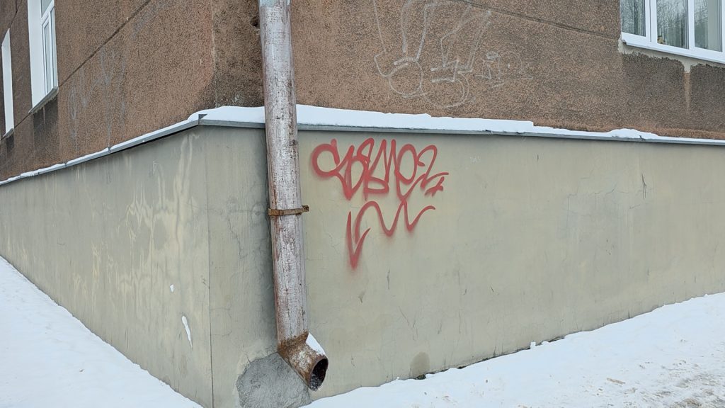 Sārts, nelegāls grafiti paraksts jeb "tegs" uz gaišas ēkas fasādes pie notekcaurules sniegotā laikā.
