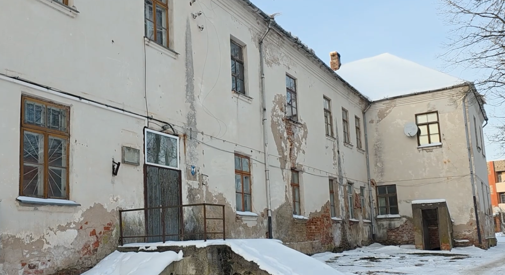 Senā Ilūkstes jezuītu klostera ēka ar nolupušu apmetumu un redzamiem sarkaniem ķieģeļiem ziemas dienā.