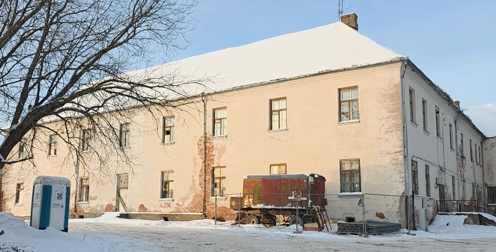 Ilūkstes jezuītu klostera fasāde ar būvlaukuma norobežojumu un pārvietojamo tualeti priekšplānā.