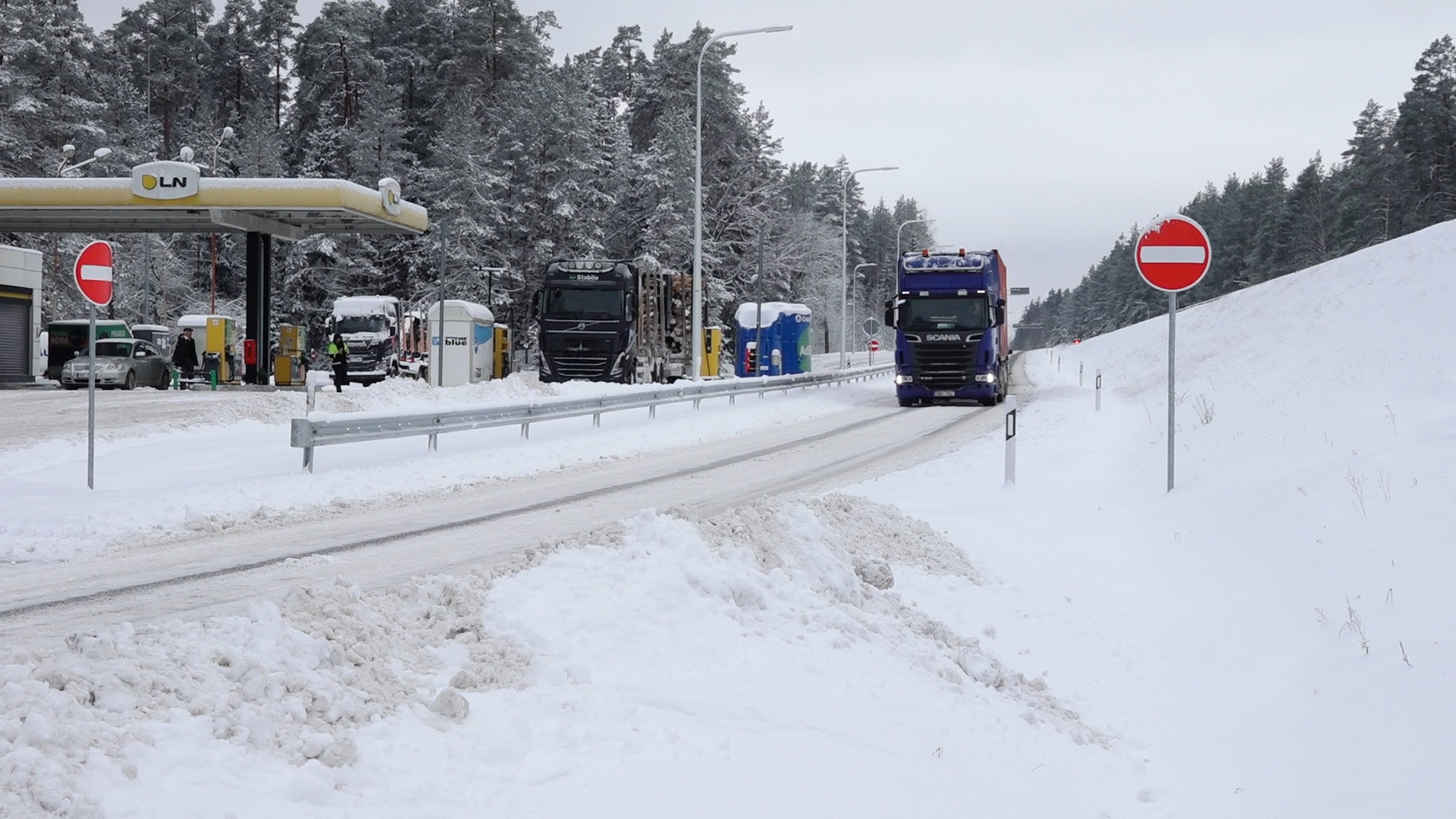 Kravas automašīnas ziemas apstākļos autoceļa malā pie degvielas uzpildes stacijas.