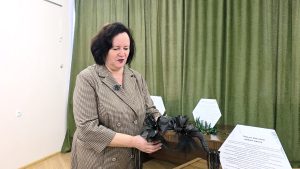 Izstādes apmeklētāja aplūko dekoratīvu melnu kroni ar spalvām un dabas elementiem