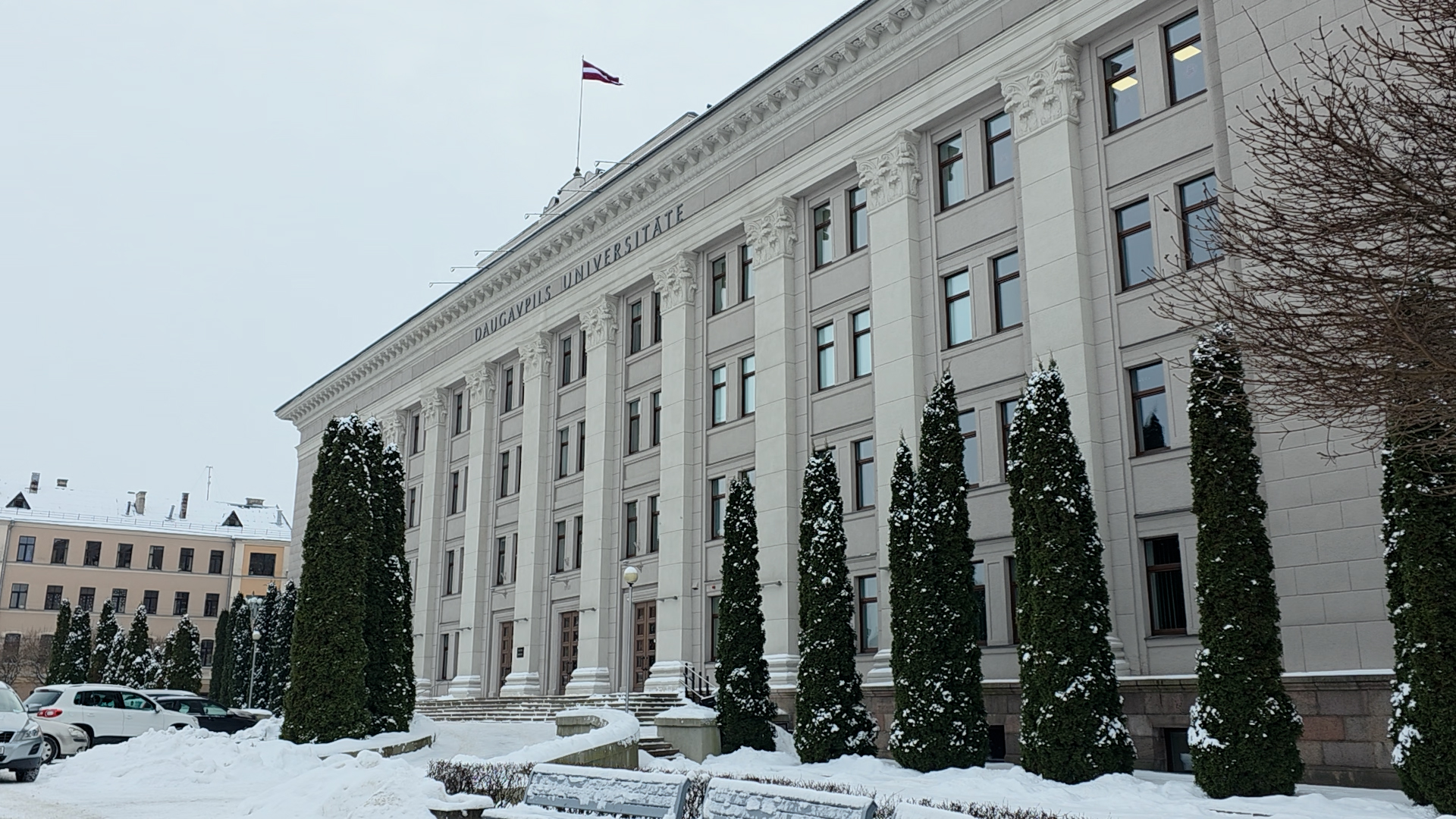 Daugavpils Universitātes galvenā ēka ziemā ar Latvijas karogu mastā.