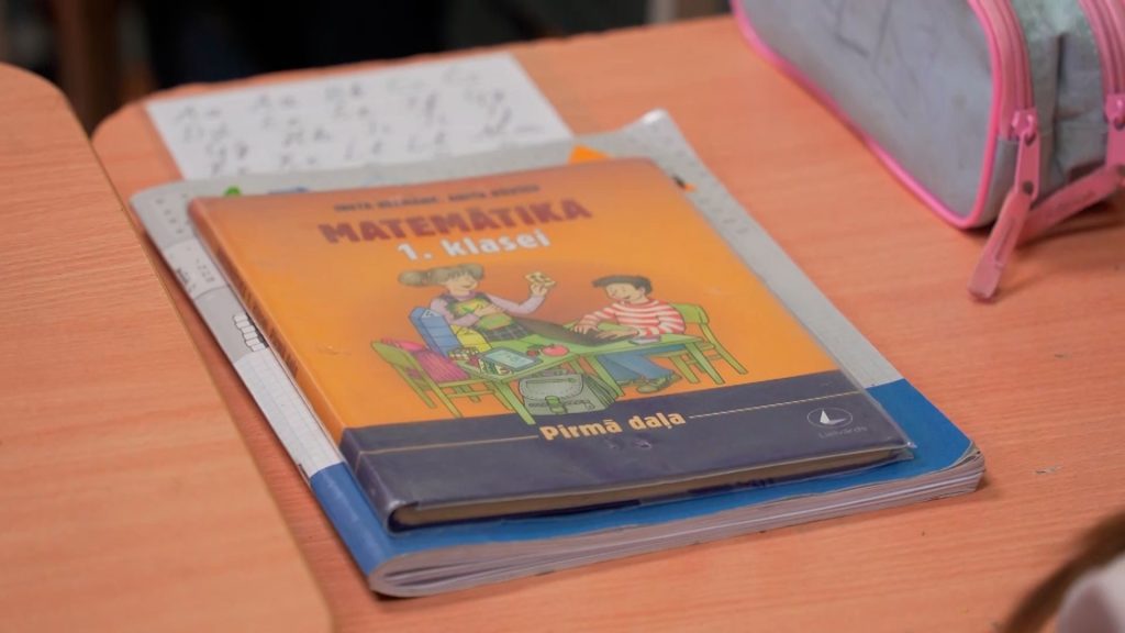 1. klases matemātikas mācību grāmata un burtnīcas uz koka skolas sola.