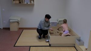 Speciālists kopā ar bērnu vada smilšu terapijas nodarbību speciāli iekārtotā telpā