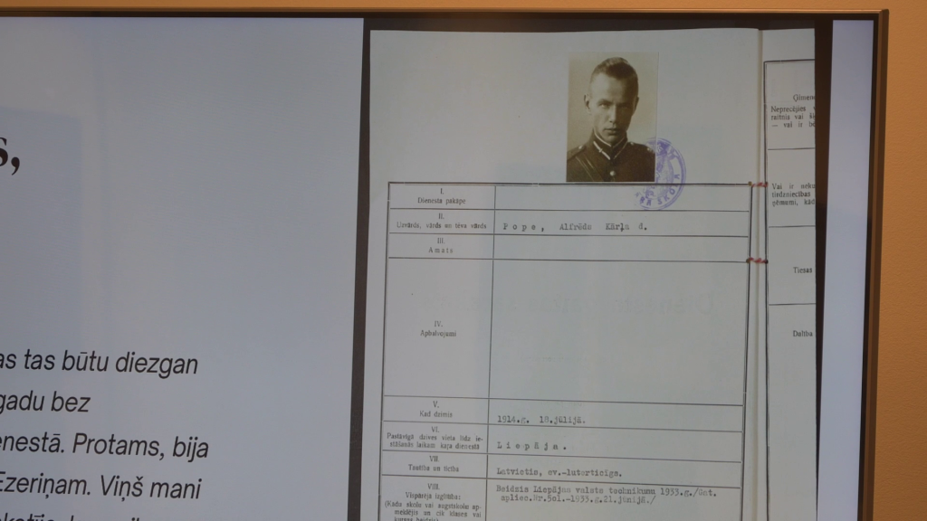 Ekrānā redzams vēsturisks dokuments ar Alfrēda Popes fotogrāfiju un dienesta informāciju mašīnrakstā.
