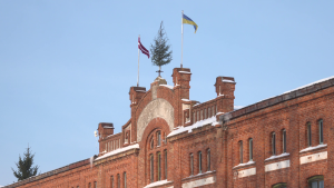 Vēsturiska sarkano ķieģeļu ēka ar Latvijas un Ukrainas karogiem ziemā