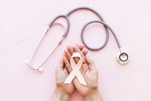 Dzemdes kakla vēža profilakses simbols – baltā lenta sievietes rokās ar stetoskopu uz rozā fona