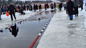 Ziemas peldētājs peld āliņģī sacensību trasē, kamēr apkārt stāv skatītāji.
