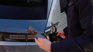 Cilvēks ar viedtālruni uzsāk elektroauto uzlādi
