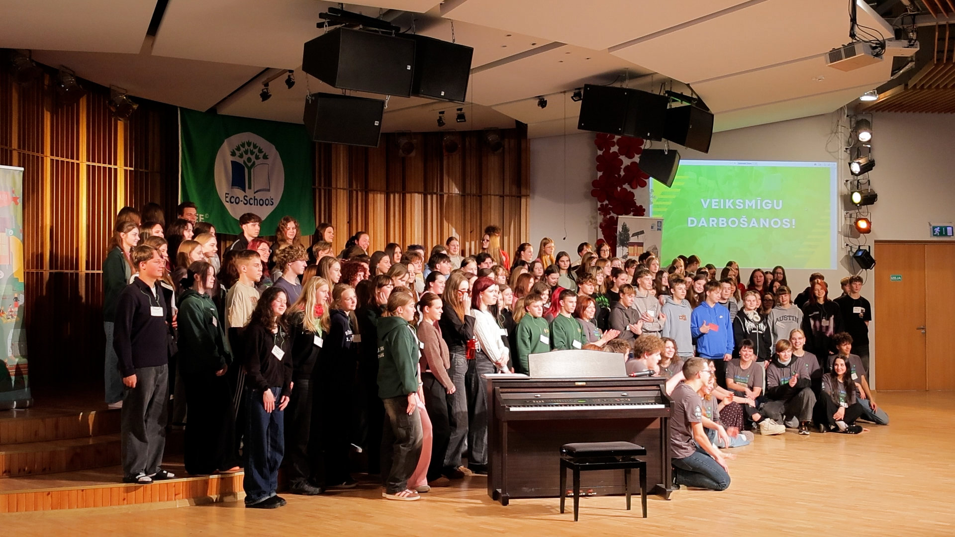 Ekoskolu Ziemas forums Jelgavā – jaunieši un pedagogi pulcējušies uz skatuves ar “Eco-Schools” karogu fonā.