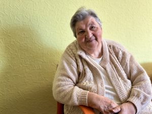 84 gadus vecā Eleonora sociālās aprūpes centra telpās, smaidot kamerai.