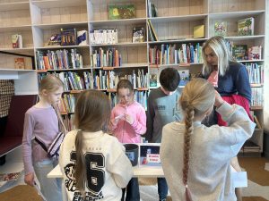 Bērni bibliotēkā piedalās izglītojošā nodarbībā par drošu interneta lietošanu bibliotekāres vadībā.