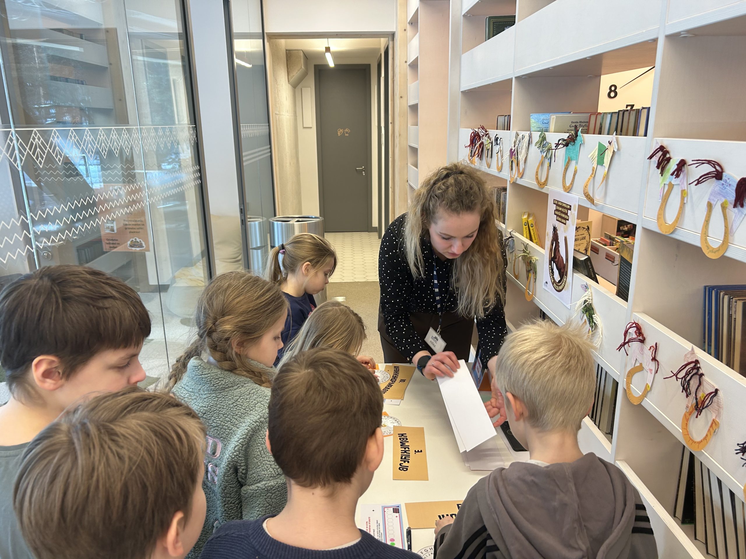 Bērni piedalās izglītojošā nodarbībā par drošu interneta lietošanu bibliotēkā kopā ar bibliotekāri.
