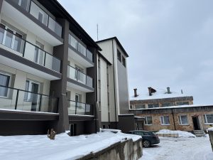 Jauna daudzdzīvokļu ēka ziemā ar balkoniem un blakus esošu ēku