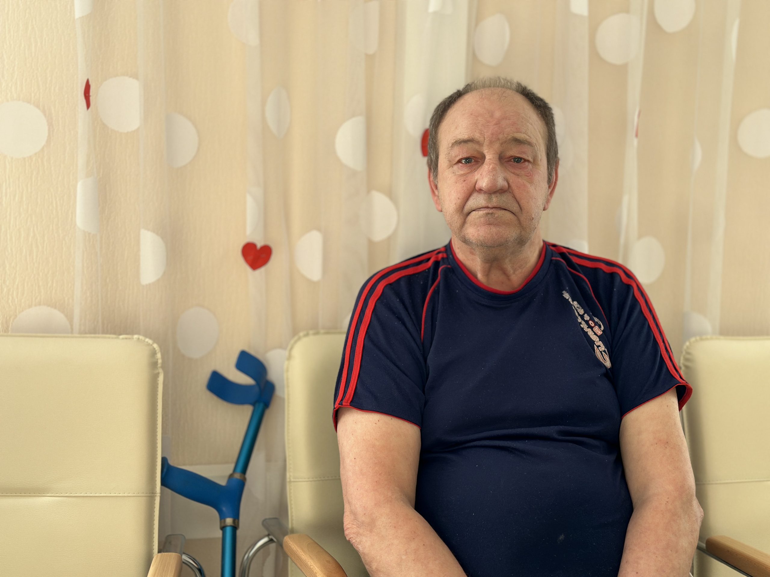 Seniors sēž krēslā telpā ar Valentīndienas dekorācijām fonā
