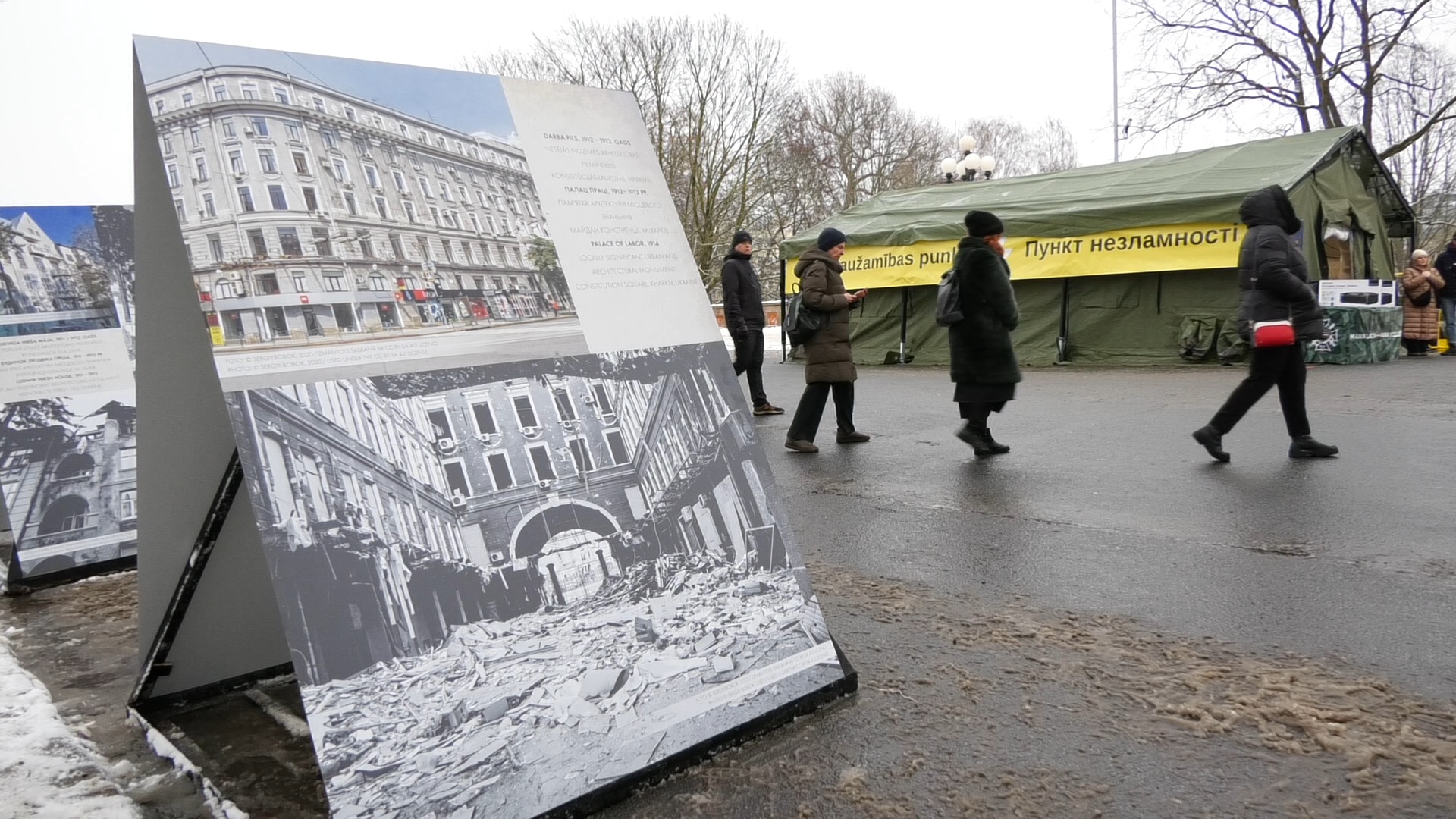 Izstādes stends ar kara postījumu fotogrāfijām Rīgā un “Nesalaužamības punkta” telts fonā
