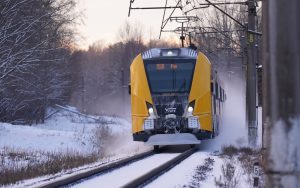Dzeltenais pasažieru vilciens brauc pa sliedēm ziemas apstākļos ceļā uz Rīgu